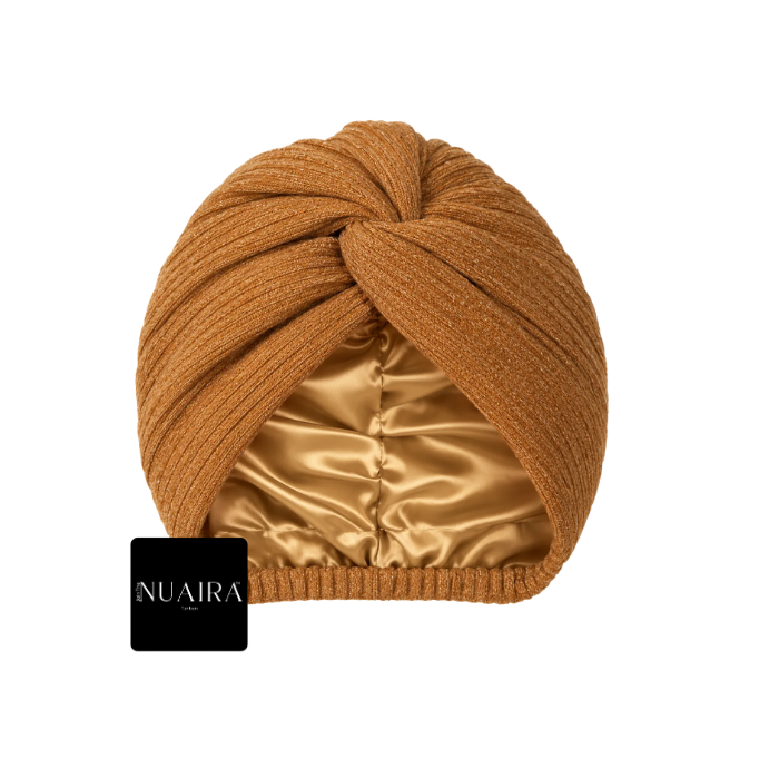 A mustard twisted knit turban-style beanie in a warm camel brown color, featuring a shiny satin inner lining and a small black brand tag on the side, set against a plain white background.