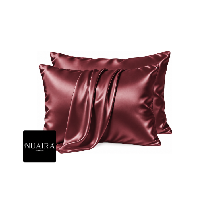 Two satin pillowcases in a deep burgundy color, draped to show off their smooth, lustrous texture, with a black brand NUAIRA