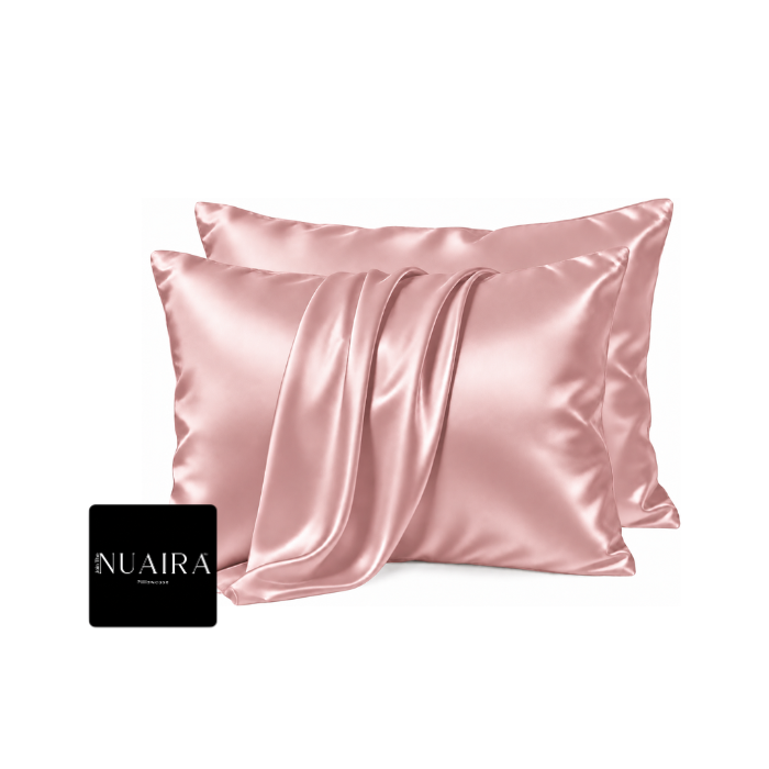 Two satin pillowcases in a soft blush pink color, styled with draped folds on a clean white background by 'NUAIRA'
