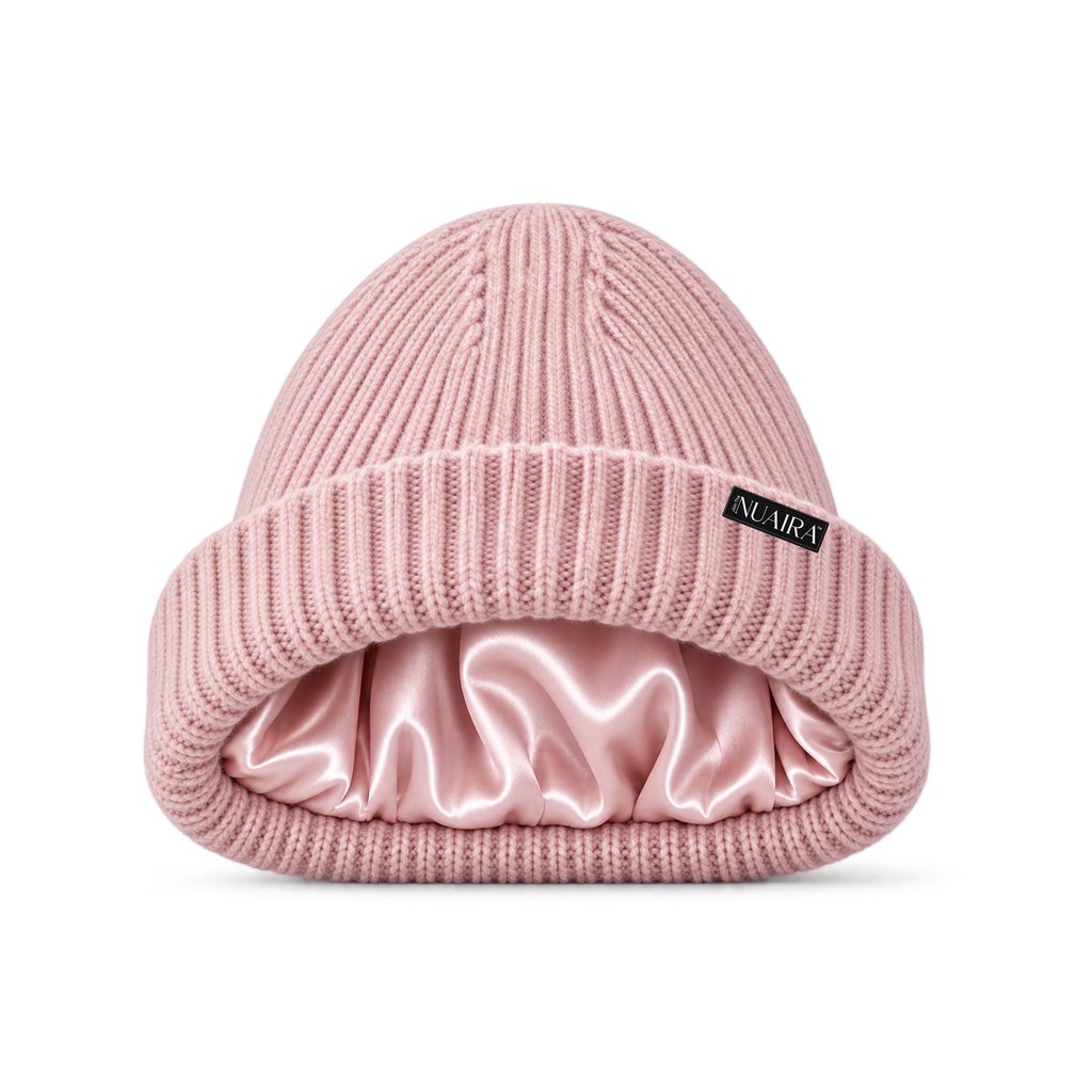 A pink ribbed knit beanie hat with a shiny pink satin inner lining, shown on a white background with a pink NUAIRA brand tag in the lower left corner.